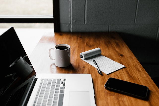 a notepad, coffee, and cell phone next to a laptop